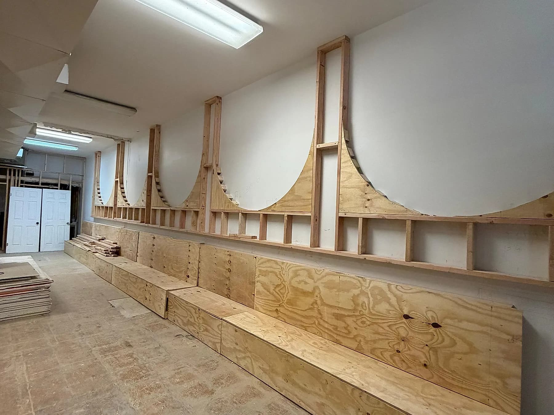 A run of banquette bases and scalloped arch panels built up in bare plywood