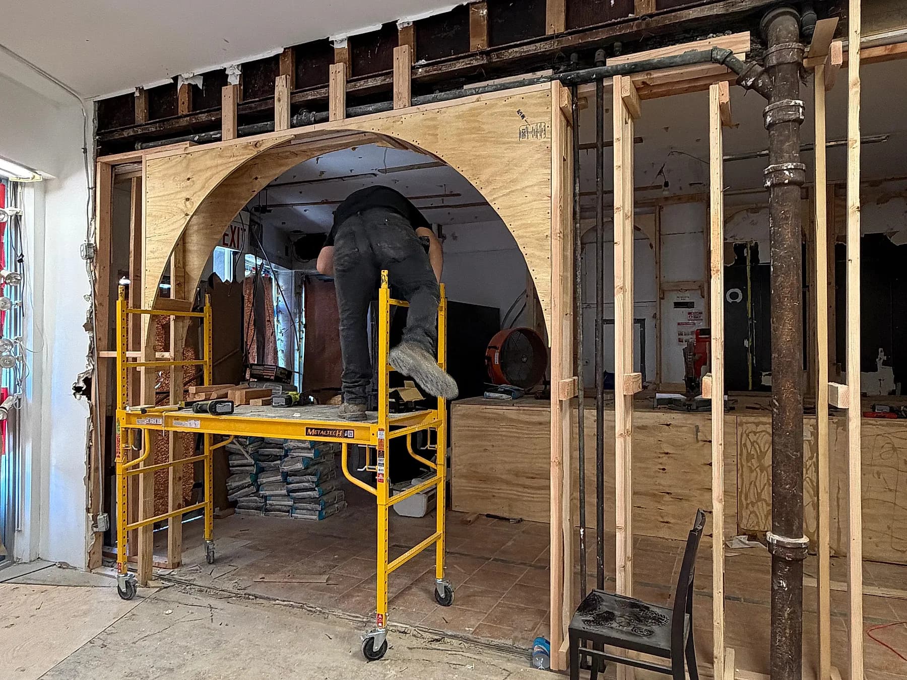 A structural arch opening cut through a masonry wall, shored with timber and a mobile scaffold tower
