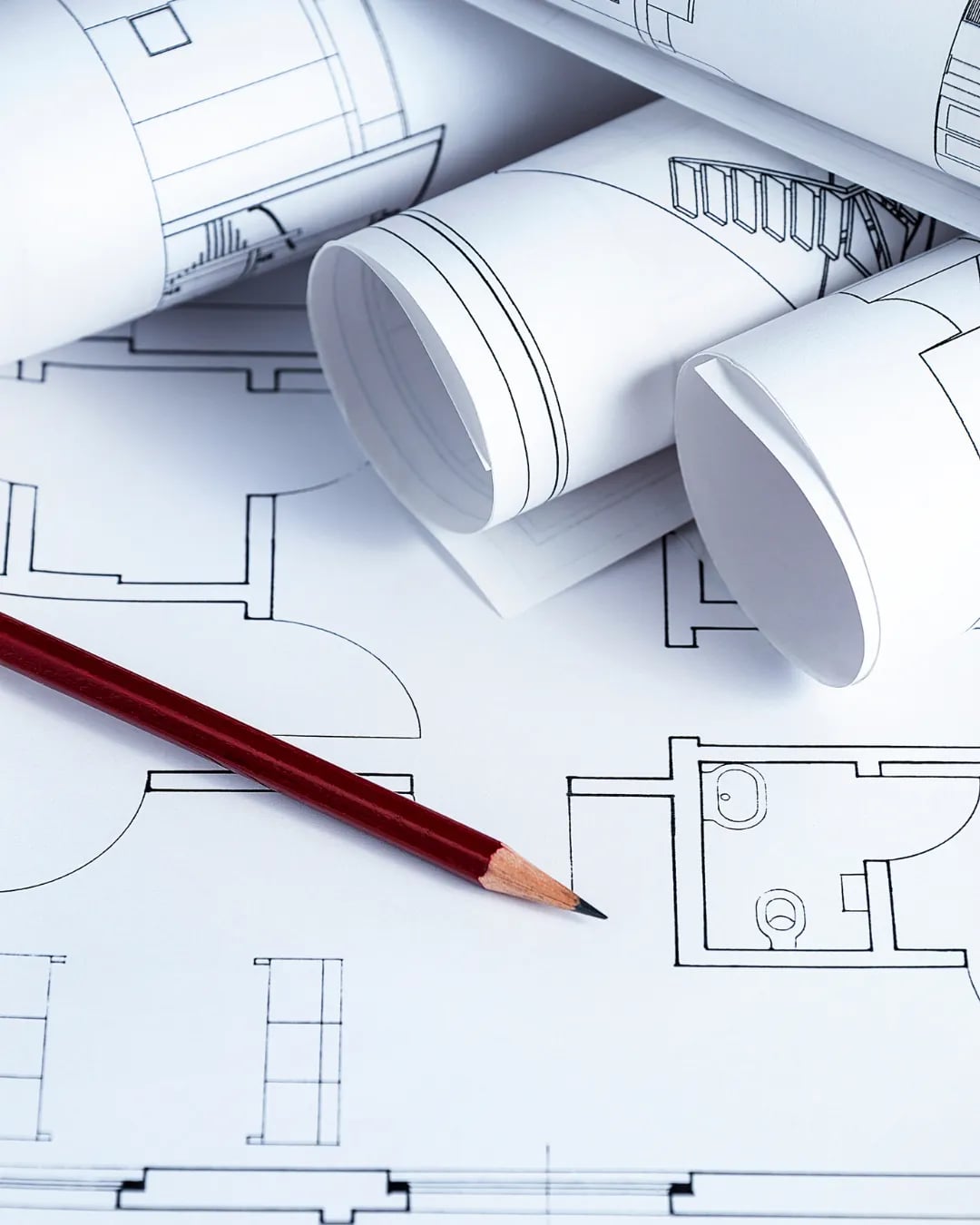 Rolled architectural blueprints with a pencil resting on a floor plan